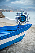 A traditional blue wooden fishing boat on a serene beach in Nerja, Spain.