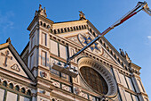 Workers on a lift clean the facade of the Basilica of Santa Croce or Basilica of the Holy Cross in Florence, Italy.