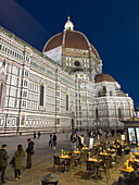 People dining al fresco in the Piazza del Duomo while tourists look at the Duomo in Florence, Italy.