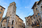 The Piazza della Cisterna & the Devil's Tower or Torre del Diavolo in the medieval city of San Gimignano, Italy. At right is the Palazzo Tortoli wiht its arches & pillars.