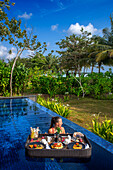 Young happy woman with a floating breakfast in the pool in the The residence luxury resort, Bintan island, Riau islands, Indonesia