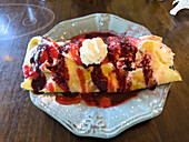 A gluten-free sweet crepe topped with whipped cream, raspberry sauce and lemon zest.