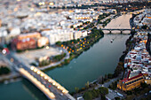 Sunset casts a warm glow over the Rio Guadalquivir and Triana Bridge in Seville, showcasing the city's vibrant architecture and life.