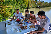 Dining inside the boat. Canal du Midi at Capestang Aude South of France southern waterway waterways holidaymakers queue for a boat trip on the river, France, Europe