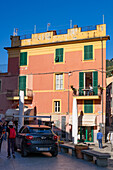 A woman sits on the balcony of a colorful building in Monterosso al Mare, Cinque Terre, Italy.