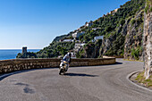 Torre a Mare, a Saracen tower and a motorcyclist on the winding Amalfi Coast road at Praiano, Italy.