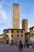 Tourists on the Piazza del Duomo with its towers in the medieval walled city of San Gimignano, Italy. L-R: Torri Salvucci and Torre Pettini.