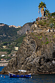 Ein kleines Fischerboot liegt im kleinen Hafen des Fischerdorfs Manarola in den Cinque Terre, Italien. Die Touristen befinden sich auf dem Aussichtspunkt darüber.