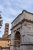 West face of the Arch of Titus in the Roman Forum in the Colosseum Archaeological Park, Rome, Italy. Behind is the bell tower of the Basilica of Santa Francesca Romana.