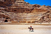 Roman Theater in the ruins of Petra, Jordan. Carved Amphitheater Theater Siq Petra Jordan. Theater built in Treasury built by the Nabataens in 100 AD, and the Romans added to it. The theater is produced from the red stone and seats up to 7,000 people. Bedouins on a donkey in front of the amphitheater of Petra.