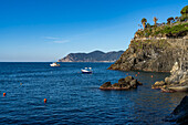 Fischerboote vor der zerklüfteten Küste der Stadt Manarola in den Cinque Terre, Italien. Touristen befinden sich auf einem Aussichtspunkt rechts.