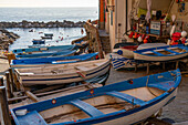 Small rowboats stored out of the water with the harbor behind in Riomaggiore, Cinque Terre, Italy.