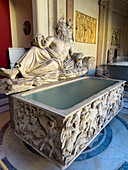 Ornately carved Roman sarcophagus with statue of Arno in the Vatican Museums, Vatican City, Rome, Italy. The scene on the sarcophagus depicts a battle between the Greeks and the Amazons.