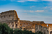 A jet airliner flying over the ruins of the Colosseum in Rome, Italy.