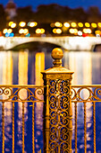 Intricate ironwork balustrade of Triana Bridge with colorful light reflections in a serene nighttime setting.