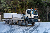 A truck hauling a huge marble block exits a tunnel in the marble quarries of Fantiscritti. Carrara, Italy. Note the road coated with marble dust and the four steering tires for negotiating tight turns.