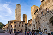 Tourists on the Piazza del Duomo with its towers in the medieval walled city of San Gimignano, Italy. L-R: Torri Salvucci, Torre Pettini and Torre Chigi.