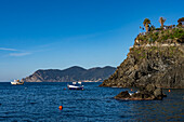 Fishing boats off the rugged coast of the Cinque Terre town of Manarola, Italy. Tourists are on an overlook at right.