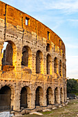 The ancient Roman Colosseum or Flavian Amphitheater with golden sunset light in Rome, Italy.