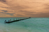 Blick auf einen Steg im türkisfarbenen Wasser vor dem Strand eines Resorts in Cayo Guillermo mit einem stimmungsvollen Himmel; Cayo Guillermo, Kuba.