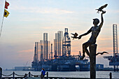 High Tide bronze statue by Charles Parks, oil platform beyond at sunset, Galveston, Galveston island, Gulf of Mexico, Texas, United States of America