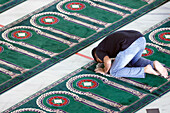 Al Akbar Surabaya National Mosque, Muslim man praying on carpet with arch design pointing towards Mecca, Surabaya, Java, Indonesia