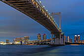 Blick auf die Regenbogenbrücke und Koto City im Hintergrund in der Abenddämmerung, Minato City, Tokio, Honshu, Japan