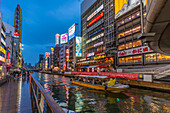 View of tour boat and colourful adverts in Dotonbori, vibrant entertainment district near the river at dusk, Osaka, Honshu, Japan