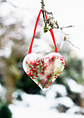 Selbstgemachter Eis-Anhänger in Herzform mit Berberitzen-Beeren und Tannenzweigen