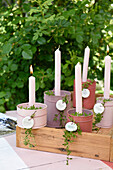 Bunt lackierte Blechdosen mit Kerzen, Thymian und Anhängern auf Holtablett im Garten