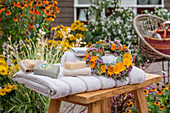 Blumenkranz aus Ringelblumen mit Seife, Bürste, Handtücher am Gartenteich vor Blumenbeet 