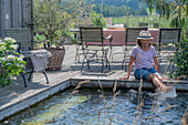 Schwimmteich und Sitzplatz auf sommerlicher Terrasse mit Olivenbaum und Hortensie im Topf 