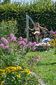 Frau unter Gartendusche neben Liegestuhl, Hohe Flammenblume (Phlox paniculata), Sonnenauge (Heliopsis helianthoides) im Beet 