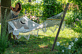 Frau befestigt Hängematte unter Sommerlinde in sommerlichen Garten