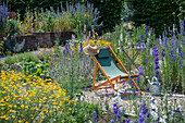 Deckchair between delphinium (Delphinium) and dyer's chamomile (Anthemis tinctoria) in the summer garden