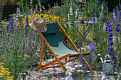 Deckchair between delphinium (Delphinium) and dyer's chamomile (Anthemis tinctoria) in the summer garden