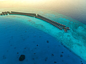 Luftaufnahme von Bungalows entlang des Riffs bei Sonnenuntergang auf dem Baa Atoll, Kanifushi Island, Malediven