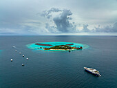 Luftaufnahme einer kleinen paradiesischen Insel mit Segelbooten entlang des Riffs, Malediven Archipelagos