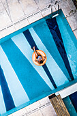 Aerial View Of Tanned Woman Floating Comfortably On Orange Inflatable Blow Up Ring In Luxury Villa Swimming Pool