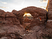 Aerial view of majestic rock formations and a natural arch at sunset with hikers in the foreground,Moab,United States
