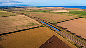 Luftaufnahme von ausgedehntem Ackerland und Bahngleisen entlang der Küstenlinie unter blauem Himmel mit Wolken, Fenham, Vereinigtes Königreich