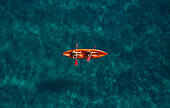 Aerial view of two sporty girls paddling on an orange kayak surrounded by a turquoise sea in Montepaone,Calabria,Italy