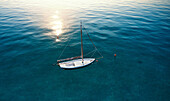 Aerial view of a tiny yet beautiful sail boat at dawn surrounded by a transparent blue sea with sun reflections in the Ionian Sea,Calabria,Italy