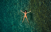Aerial view of a beautiful woman wearing an orange bikini while floating and sunbathing in a transparent sea in San Sostene,Calabria,Italy