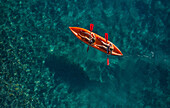 Aerial view of two sporty girls paddling on an orange kayak surrounded by a turquoise sea in Montepaone,Calabria,Italy