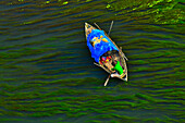 Sirajganj,Bangladesh - 23 December 2018: Aerial view of two person on a wooden canoe crossing a river full of algae in Sirajganj,Bangladesh