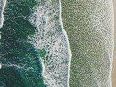 Aerial view of surfers in the sea walking through the waves in Peniche,Portugal 