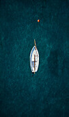 Aerial view of a tiny yet beautiful sail boat at dawn surrounded by a transparent blue sea moored in the Ionian Sea,Calabria,Italy