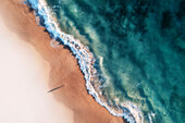 Aerial view of a white sandy beach with white waves rolling onto shore and crystal clear blue water and a girl standing on the beach casting a long shadow,Port Noarlunga,South Australia,Australia