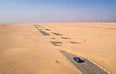 Luftaufnahme eines Autos, das auf einer mit Sand bedeckten Straße in der Wüste von Dubai fährt,V.A.E